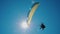 Extreme paraglider flying against a clear blue sky, sunbeam shines into camera