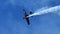 Extreme stunt plane with black wings flying in the blue sky with white smoke