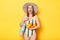 Extremely amazed woman wearing striped swimsuit and straw hat  yellow background standing with bag and fresh oranges