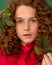 Extremely close-up portrait of teenage girl with red curly hair with freckles with green leaves in hands. Concept of natural