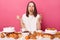 Extremely hungry brown haired woman in white t shirt breaking diet sitting at table with desserts eating different sweets isolated