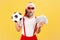 Extremely surprised shocked elderly man in santa claus hat and stylish eyeglasses holding dollar banknotes and soccer ball,