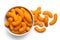 Extruded cheese puffs in a white ceramic bowl next to spilled cheese puffs isolated on white. Top view