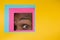 Eye of african-american man peeking throught square in yellow background