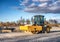 Eye catching yellow road roller with enclosed climate controlled cabin stands on not ready new road, stones, blue sky, clouds,