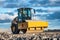 Eye catching yellow road roller with enclosed climate controlled cabin stands on not ready new road, stones, blue sky, clouds,