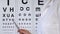 Eye doctor pointing at letters for spelling to person at medical examination