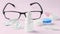 Eye dropper with contact lens, eyeglasses and accessories on pink background