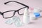 Eye drops with contact lens, eyeglasses and accessories on pink background