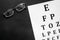Eye examination. Eyesight test chart and glasses on black background top view copy space