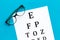 Eye examination. Eyesight test chart and glasses on blue background top view