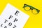 Eye examination. Eyesight test chart and glasses on yellow background top view