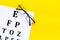 Eye examination. Eyesight test chart and glasses on yellow background top view copy space