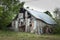 Eye-level shot of an old wooden decrepit barn standing near green trees