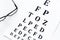 Eye test, eye examination. Glasses with transparent optical lenses on eye test chart on white background top view