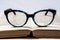 Eyeglasses with blue frame on open book showing clear text on white background. Reading learning concept