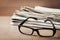 Eyeglasses and stack of newspapers on wooden desk for themes of ophthalmology, poor vision and reading