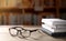 Eyeglasses with stacked books and black laptop on wooden table in library