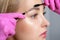 Eyelash artist plucks eyebrows with tweezers. Beautiful blonde woman having Permanent Make-up Tattoo on her Eyebrows. Professional
