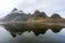 Eystrahorn mountain peaks with fog around and beautiful reflections in the calm lake.