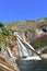 Ezaro cascade and Xallas river. Waterfall with colorful rocks and blue sky.  Dumbria, Spain.