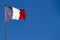 Fabric textile tricolor flag of France with blue, white and red stripes fluttering in the wind with copy space in sunny