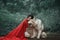 Fabulous image, dark-haired brunette attractive lady in short white dress, long red scarlet cloak lying on ground sits