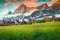 Fabulous mountain resort in the Dolomites, colorful spring flowers with high misty mountains and cute wooden houses at sunset, San
