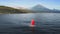 Fabulous scarlet red sail white Jukung boat floating on ocean water near sea shore with huge volcano in summer. Idyllic