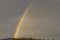 Fabulous view of rainbow in cloudy summer evening sky over tops of forest trees.