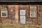 Facade of an abandoned wooden old house with dilapidated door and rusty windows with bars