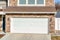 Facade of attached garage with wide white garage door against stone brick wall