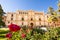 Facade of the building of the College of Saint Ildefonso, seat of the University of Alcala de Henares and rose garden in the