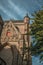 Facade and church tower made of bricks, roofs and leafy tree with blue sky at Bruges.