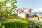 The facade of a classic Mediterranean two-storey cottage in the spring. In front of the cottage there is a green lawn