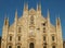 Facade of the Duomo Cathedral in Milan against blue sky, lit by golden setting sun