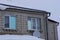 Facade of a gray private brick house with windows with a roof under white snow