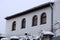 Facade of a gray private house with windows with a roof under white snow against the sky