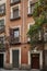 Facade of a narrow building built with exposed clay brick, balconies with wrought iron railings and a portal with a wooden door