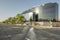 facade of an office building covered in shiny looking steel and glass forming a curve and a rectangle and trees along the street