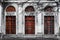 Facade of old abandoned building with three large arched windows of the red glass. Monochrome background