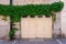 The facade of an old house with a wooden gate, overgrown with green ivy.