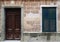 Facade of an old spanish house with dark brown wooden door in a stone frame and black closed shutters with old crumbling tiles