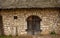 Facade of an old stone brick wall with wooden doors, a small window and thatched roof