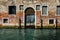 Facade of partially mossy old brick house with wooden vintage door on narrow canal in Venice, Italy.
