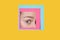 Face of caucasian woman peeking throught square in yellow background