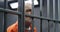 Face close up of elderly prisoner standing behind metal bars in prison cell