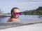 Face closeup of young woman wearing purple sunglasses looking at camera in infinity rooftop swimming pool on a sunny day over