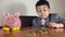 Face expression of uncomfortable preschool child, boy in suit counting the coins. Investment concept and child savings