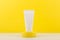 Face or hands cream in white tube on yellow podium against yellow background with copy space